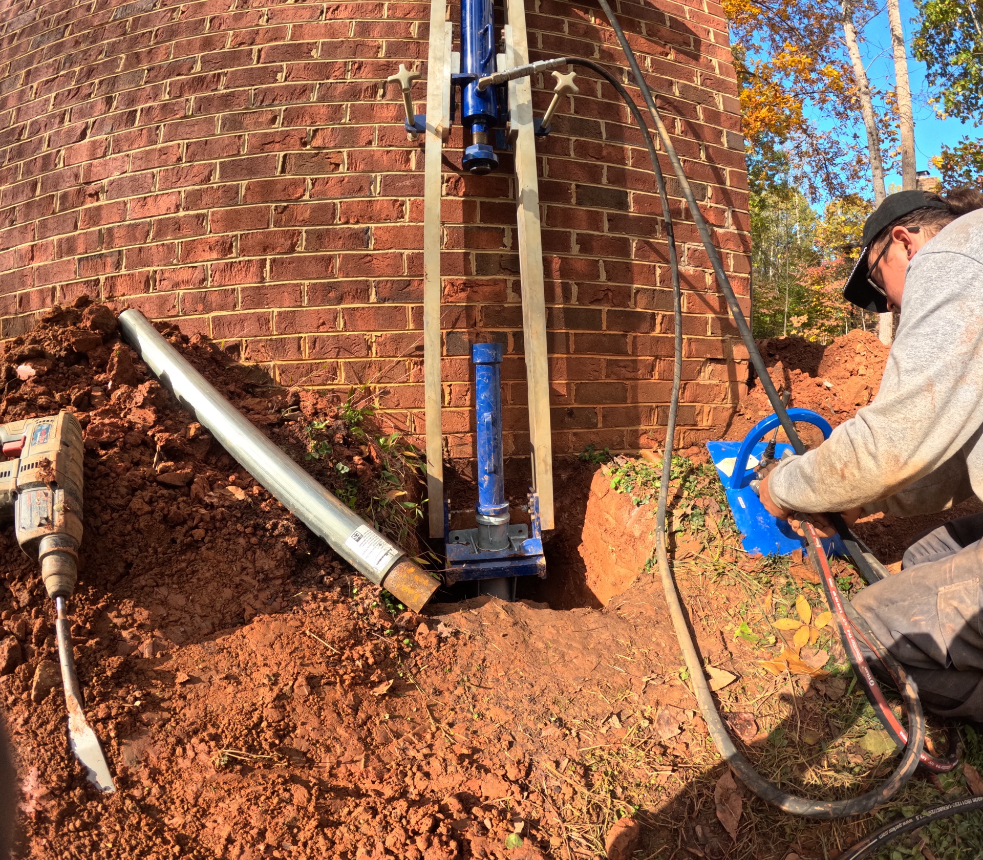 Push piers installation near brick foundation, hydraulic drive system in action.